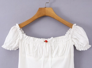 Détail du haut blanc à volants avec rose rouge au décolleté et manches bouffantes