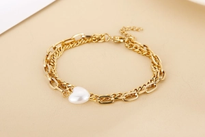Detailed macro view of a gold double-layer chain bracelet featuring a white heart pearl