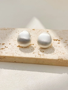 Detail of silver water drop earrings with brushed matte finish on a textured stone
