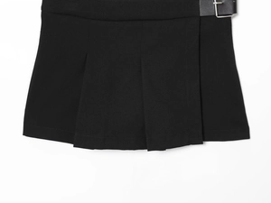 Détail de la jupe plissée noire avec ceinture à boucle métallique et texture du tissu