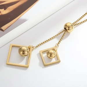 Macro view of gold box chain necklace with geometric square and polished bead pendants