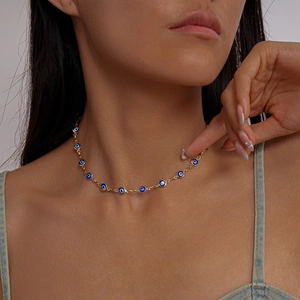 Detail of gold evil eye necklace with blue enamel charms on model neck for styling