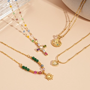 Elegante Goldene Halsketten mit Kreuz-, Muschel- und Sonnenanhängern auf beigem Hintergrund