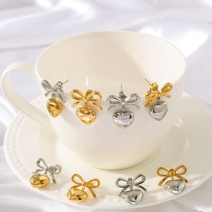 Elegant bow and heart drop earrings in 18K gold and silver displayed on a tea cup