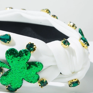 Detailed close-up of a white knotted headband with green glitter shamrock and rhinestones