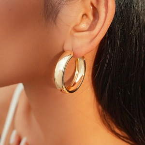 Close-up of model wearing thick golden hoop earrings with a polished metallic finish