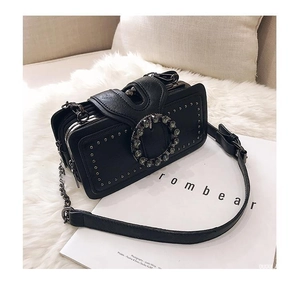 Detail of black crossbody bag featuring rhinestone buckle, studs, and chain strap