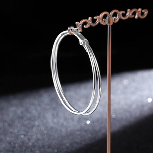 Close-up of large polished silver hoop earrings hanging on a vintage metal display stand