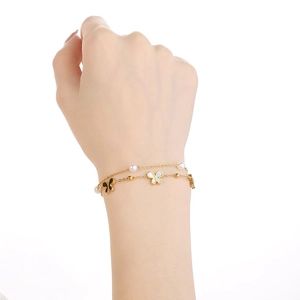 Detail of layered gold bracelet featuring white pearls and butterfly charms on wrist