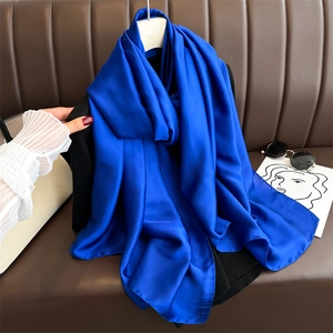 Close-up of royal blue satin scarf draped on a brown leather texture showing silky folds
