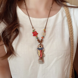 Detail of a handmade ceramic fish pendant necklace with wooden beads on a white linen shirt