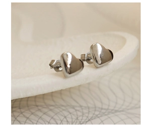 Macro close-up of polished silver heart-shaped stud earrings on white textured display