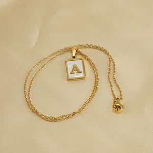 Gold stainless steel necklace with shell letter A pendant on beige satin background