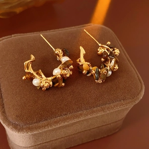 Close-up of golden C-shaped floral earrings with tiger eye stones and white pearls