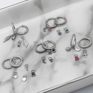 Detailed flat lay of S925 silver hoop earrings with feather and zircon charms on marble