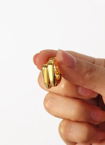 Macro view of gold-plated minimalist asymmetric earrings held between fingertips