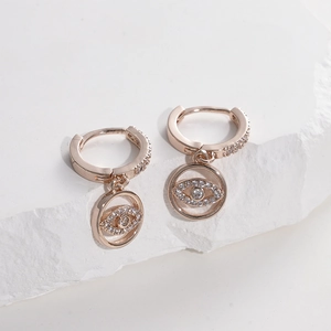 Close-up of rose gold evil eye earrings with pavé crystals on a textured stone surface