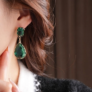 Elegant gold earrings with square and teardrop green zircon stones worn by a model