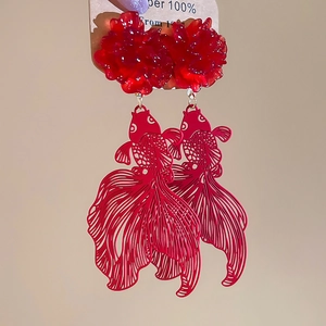 Macro detail of red resin flower and hollow goldfish dangle earring on brown card