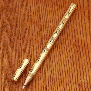 Detail of golden brass bamboo-style business pen on a dark wood grain background