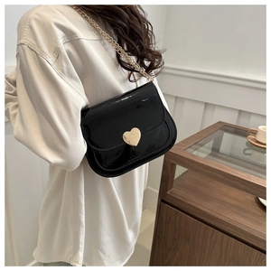 Detail of glossy black patent leather shoulder bag with golden heart buckle and chain strap