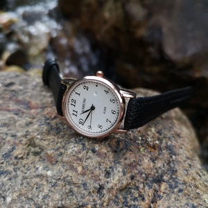 Quartz watch with rose gold case, black leather strap and calendar on natural rocks
