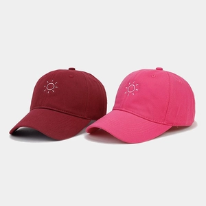 Detail of embroidered sun logo on deep red and bright pink cotton canvas baseball caps