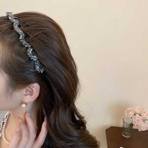 Close-up of wavy rhinestone headband and pearl earrings worn by a model in soft lighting