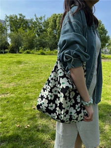 Close-up of black floral canvas tote bag with white flower prints on park grass
