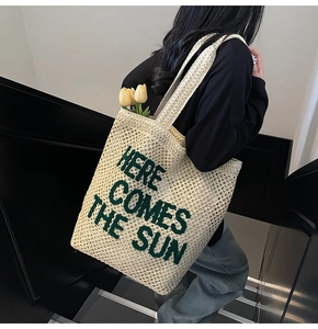 Detail of cream straw tote bag with green 'HERE COMES THE SUN' text and yellow tulips
