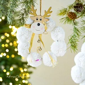 Christmas wreath with plush white balls and golden reindeer head hanging on a Xmas tree