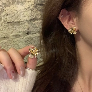Detail of gold floral earring with textured petals and a pearl accent on a model