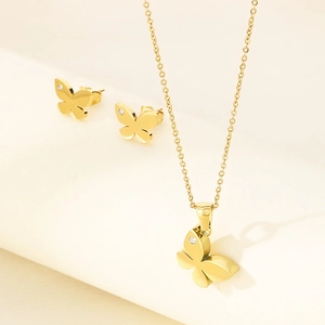 Golden butterfly pendant necklace and earrings set with sparkling zircon on beige background