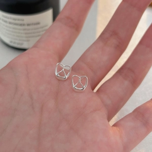 Minimalist 925 sterling silver pretzel heart stud earrings shown in hand for scale