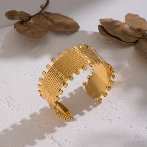 Detailed texture of gold geometric wave pattern cuff bracelet on white stone surface