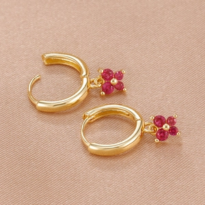 Vue macro de boucles d'oreilles dorées avec pendentifs fleur en zircon rouge sur soie
