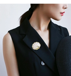 Detailed close-up of shell-shaped pearl brooch with gold edges pinned on a suit jacket