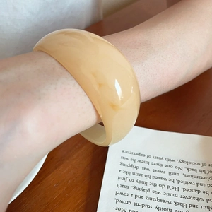 Detail of amber acrylic resin bangle with organic pleated texture worn on wrist