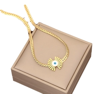 Golden Evil Eye necklace with sunburst pendant and flat Cuban chain on a jewelry box