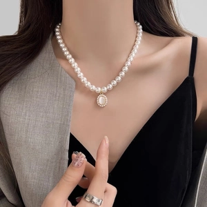 Close-up of gold pearl necklace with an oval cat eye stone and crystal cross pendant