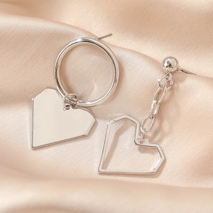Detailed close-up of asymmetric silver heart earrings on champagne satin fabric texture