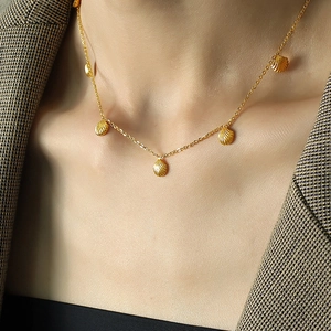 Elegant gold necklace with five small shell pendants worn over a checkered blazer