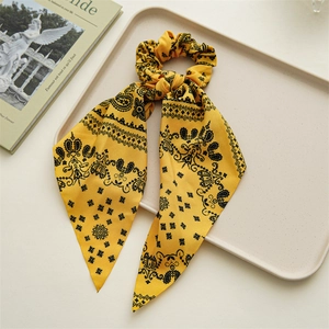 Detail of yellow paisley silk scrunchie with ribbons on a minimalist cream tray