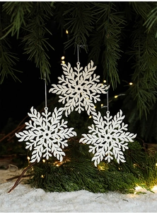 Close-up of three white snowflake ornaments hanging on green pine branches with warm lights