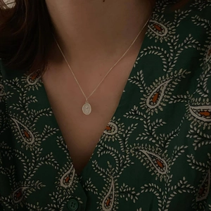 Detailed view of an oval rose relief pendant on a minimalist silver chain necklace