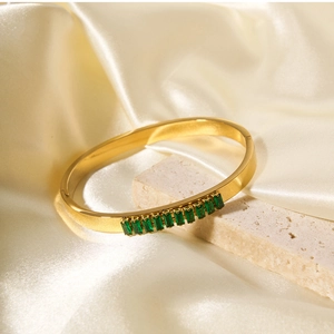 Detail of gold bracelet featuring green rectangular gemstones on a silk background
