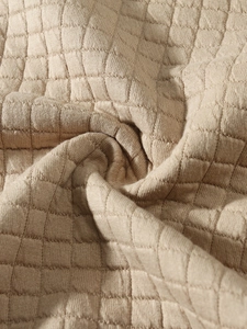 Macro view of beige knit fabric featuring a distinct textured square checkered pattern