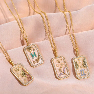 Detailed view of gold 12 zodiac necklaces with colorful enamel pendants on pink silk fabric