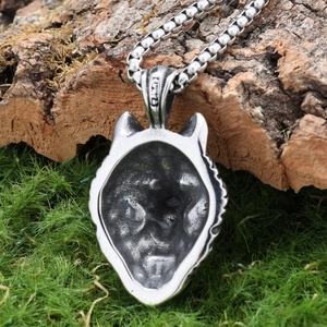 Silver wolf head pendant necklace in stainless steel shown on natural mossy bark texture