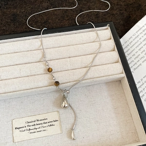 Detail of silver snake chain necklace with tiger eye bead and drop pendant in a beige box